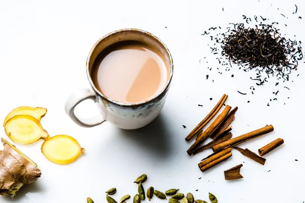 Ceramic mug of milky chai surrounded by ginger, cinnamon and cardamom
