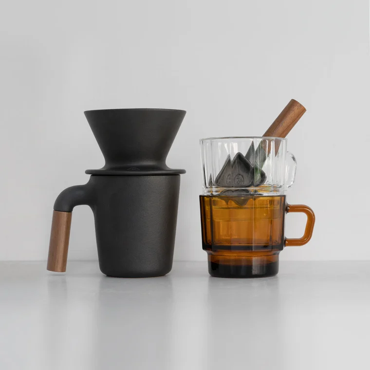 Matte black pour-over dripper with wooden handle beside amber glass cups