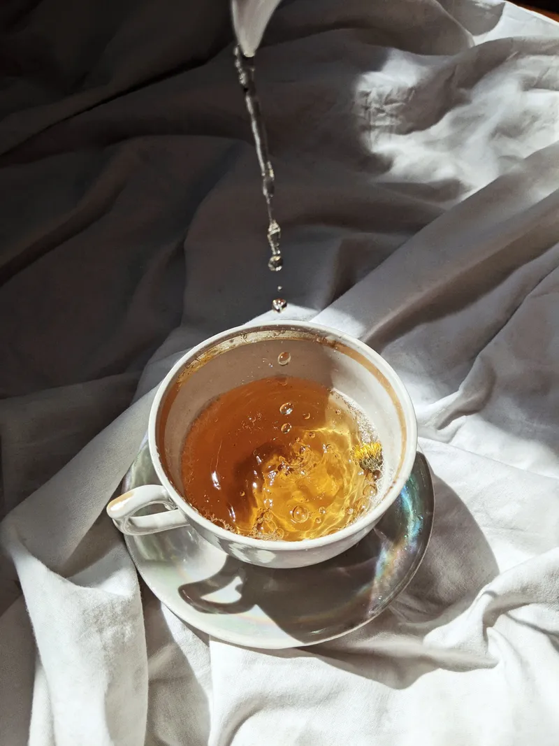 Hot water poured from a white kettle into a teacup of amber tea