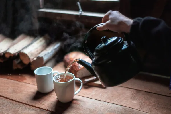 Steaming tea poured from a black kettle into a white mug